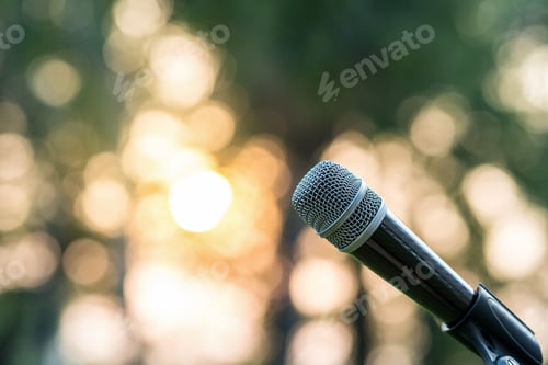 Preview: Microphone on the stage over the Abstract blurred photo of green tree with sunset light background