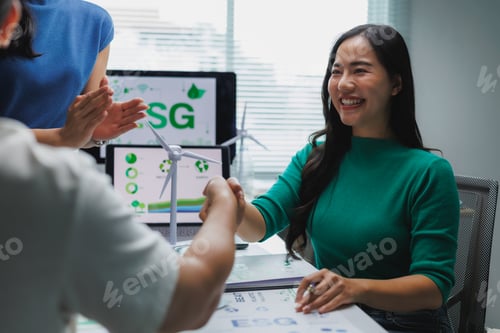 Preview: Businesswomen shaking hands over sustainable project in modern office