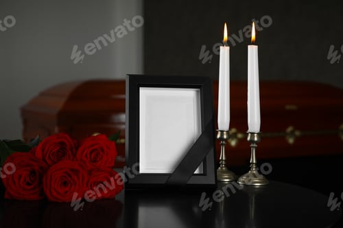 Preview: Black photo frame with burning candles and red roses on table in funeral home