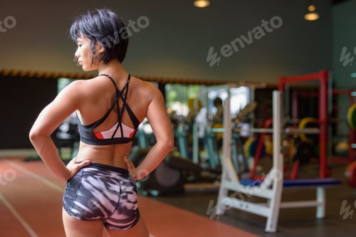 Preview: Back view of young beautiful Asian woman thinking at the gym