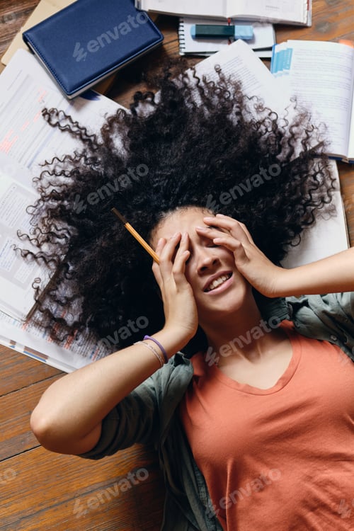 Preview: Smiling student girl lying on floor with textbooks around dreamily covering eyes with hands