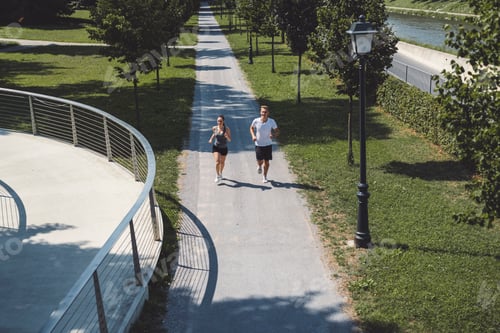 Preview: A couple jogging together on a scenic path surrounded by greenery. The path is lined with trees and