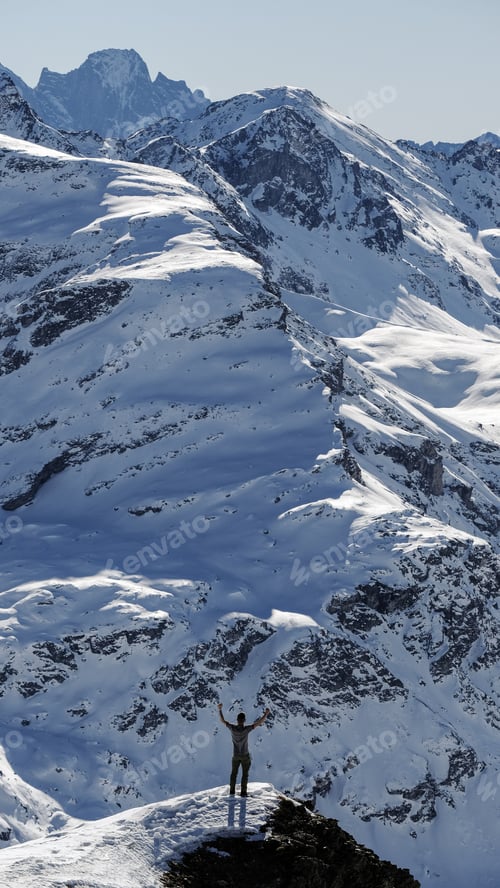 Preview: Vertical shot of a person standing in front of a snowy mountain.