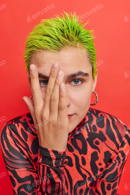 Preview: Glad style concept. Extraordinary millennial girl with green haircut looks through fingers wears cas