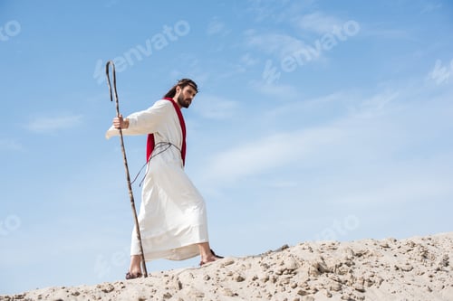 Preview: side view of Jesus in robe, red sash and crown of thorns walking on sandy hill with wooden staff in