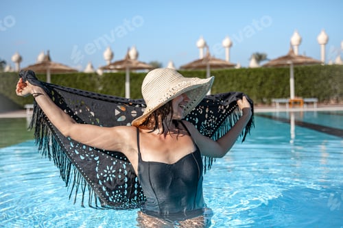 Preview: Attractive girl in a straw hat with a cape bathes in the pool close up.