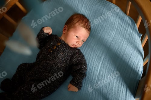 Preview: A little newborn boy is looking at the window in his crib.