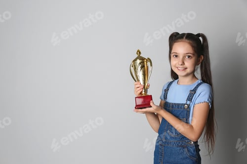 Preview: Happy girl with golden winning cup on light background. Space for text