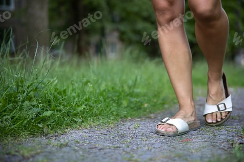 Preview: Close-up, female legs in summer sandals among the grass.