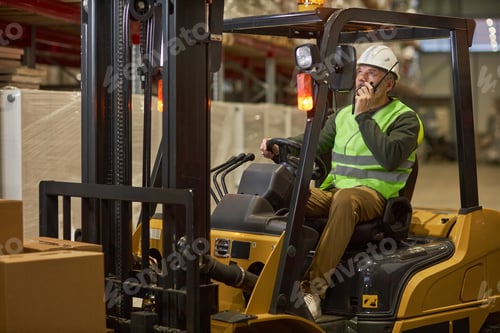 Preview: Bearded male worker driving forklift truck in warehouse