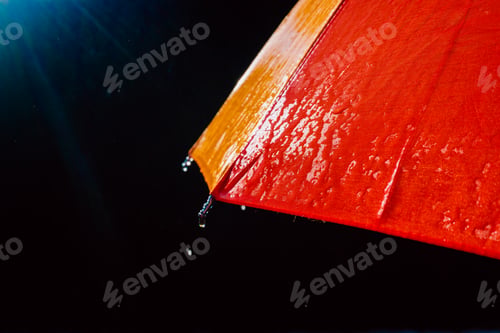 Preview: Rain on a warm-toned umbrella lit by the sun, isolated on black background with copy space.
