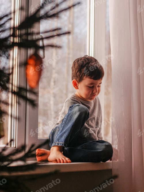 Preview: Boy sits on the windowsill and plays with a Christmas tree toy