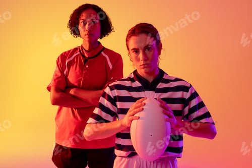 Preview: Portrait of diverse female rugby players with rugby ball over neon pink lighting