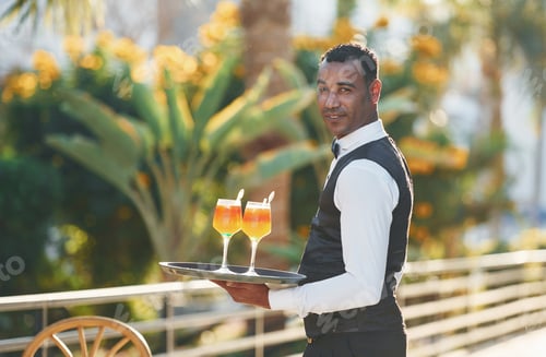 Preview: Holds cocktails. Black waiter in formal clothes is at his work outdoors at sunny daytime