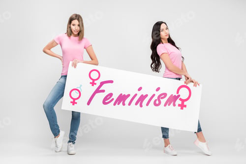 Preview: attractive women holding large sign with feminism lettering on grey background