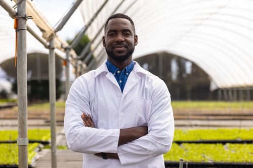 Preview: Male scientist in lab coat standing confidently in hydroponic farm greenhouse