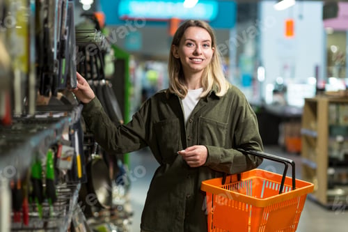 Preview: young caucasian woman walks between rows of supermarket with a basket in hands.
