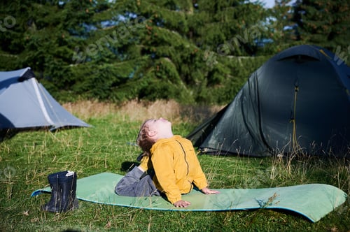 Preview: Young boy engaged in yoga pose on green mat in grassy field in the camping.