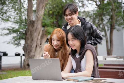 Preview: Three young people smiling and using a laptop computer while working together on a project outdoors