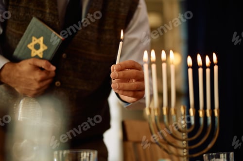 Preview: Close up of Jewish man lights candles in menorah while celebrating Hanukkah at home.