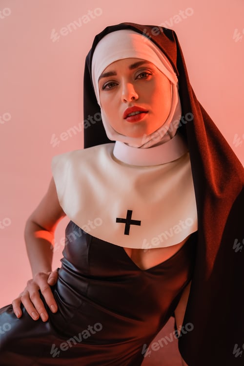 Preview: sensual nun in sexy dress looking at camera isolated on pink