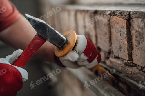 Preview: Builder's gloved hands working with hammer and chisel at the construction site