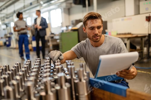Preview: Young steel worker checking quality of manufactured rod cylinders in industrial building.