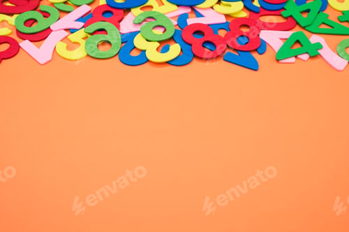 Preview: Closeup shot of the colorful wooden numbers scattered on an orange surface - space for text