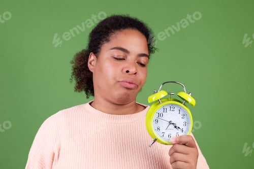 Preview: Beautiful african american woman on green background with alarm clock angry tired unhappy