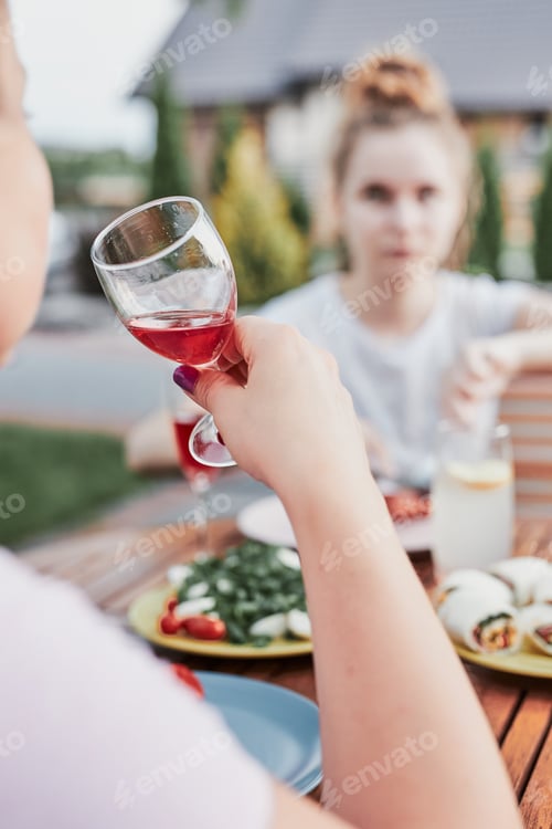 Preview: Woman drinking red wine during summer outdoor dinner in a home garden. Close up of hand holding wine