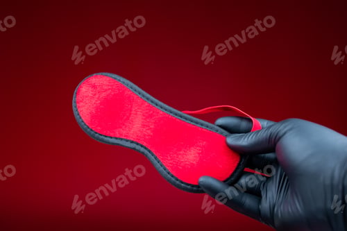 Preview: hands in black gloves holding a red erotic bandage for bdsm games