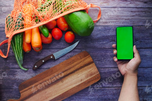 Preview: top view of man's hand holding smart phone with fresh vegetable on table