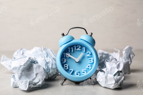 Preview: Crumpled paper balls and alarm clock on grey table