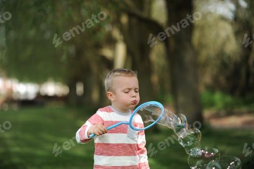 Preview: Little boy blowing huge soap bubbles in park in summer