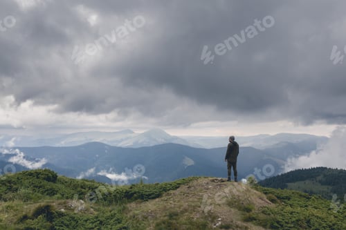 Preview: The man standing on the mountain against rainy clouds