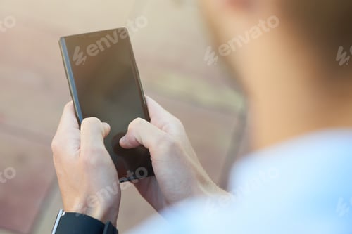 Preview: Rear view of a man using smartphone while spending time outdoors, focus on mobile phone