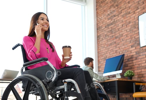 Preview: Young woman in wheelchair talking on smartphone at office
