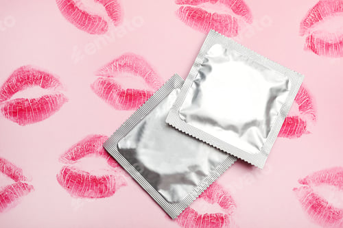 Preview: Condoms with lipstick kiss marks on pink background, flat lay. Safe sex