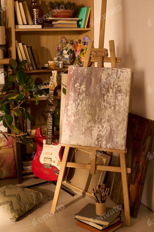 Visualização: Empty Canvas on Easel Standing in Cozy Artist Studio with Guitar and Books