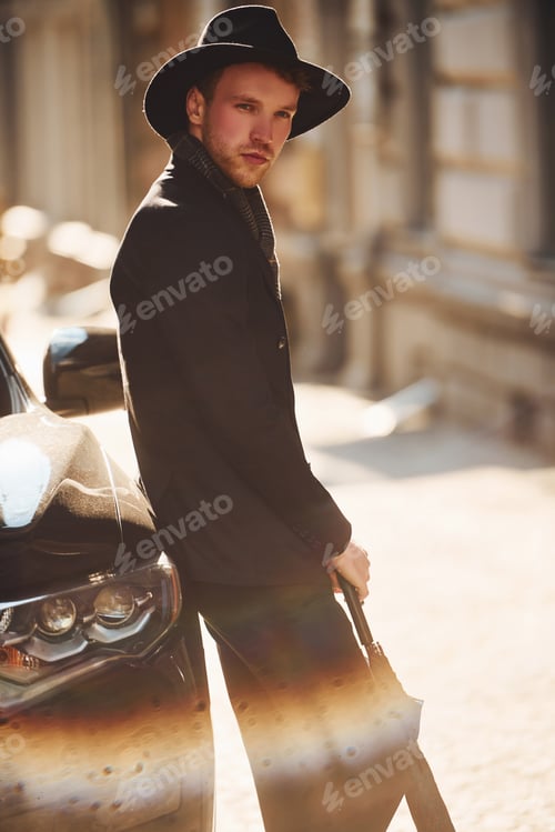 Preview: Standing near black car. Elegant young man in formal classy clothes outdoors in the city