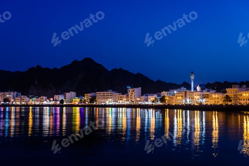 Preview: The city of Muscat, waterfront lights, mountains behind, at night