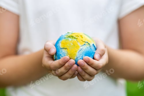 Preview: Kid holding small planet in hands against spring or summer green background. Ecology, environment