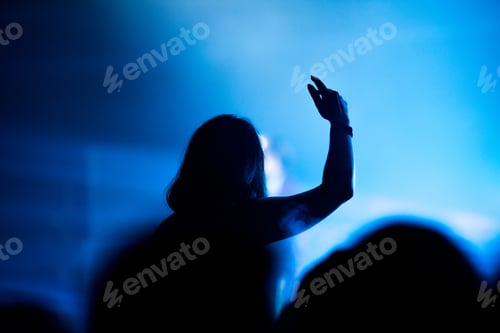 Preview: Rear view of crowd with arms outstretched at concert. Bright stage lights in the background