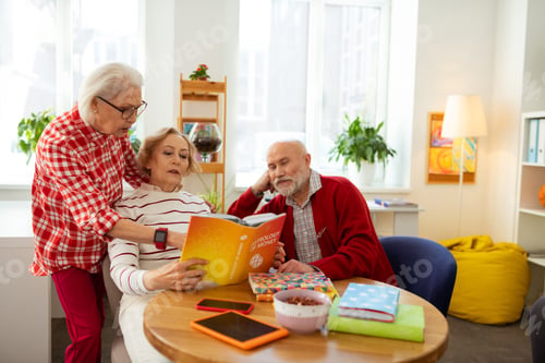 Preview: Read Here. Pleasant Aged Woman Pointing At The Book While Standing Behind Her Friend