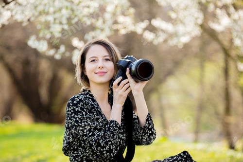 Preview: Young girl with camera sitting near a flowering tree i