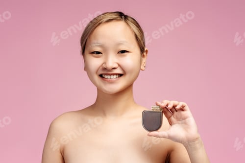 Preview: Smiling Asian girl with bare shoulders holding cardiac pacemaker, looking at camera, isolated