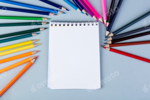 Preview: top view of a sketchbook with colored pencils arranged around on white background