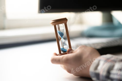 Preview: a businessman sitting on the workplace, hand holding hourglass as the time is money concept