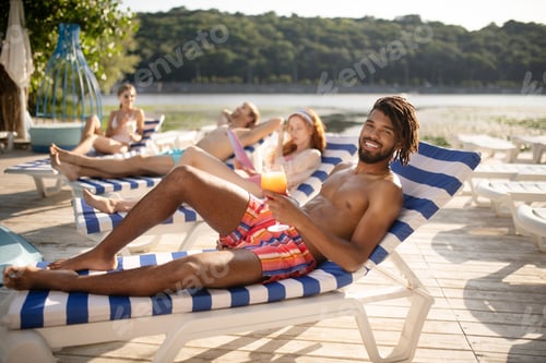 Preview: Handsome dark-skinned man drinking cold cocktail and sunbathing
