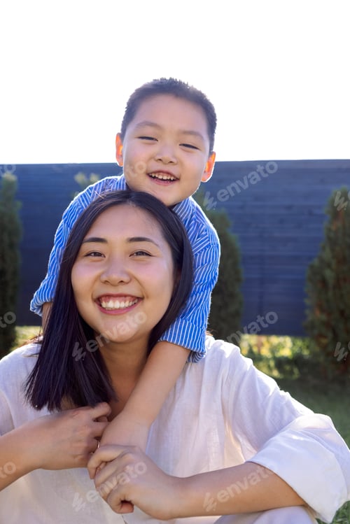 Preview: Asian laughing mom and son are hugging on a green lawn